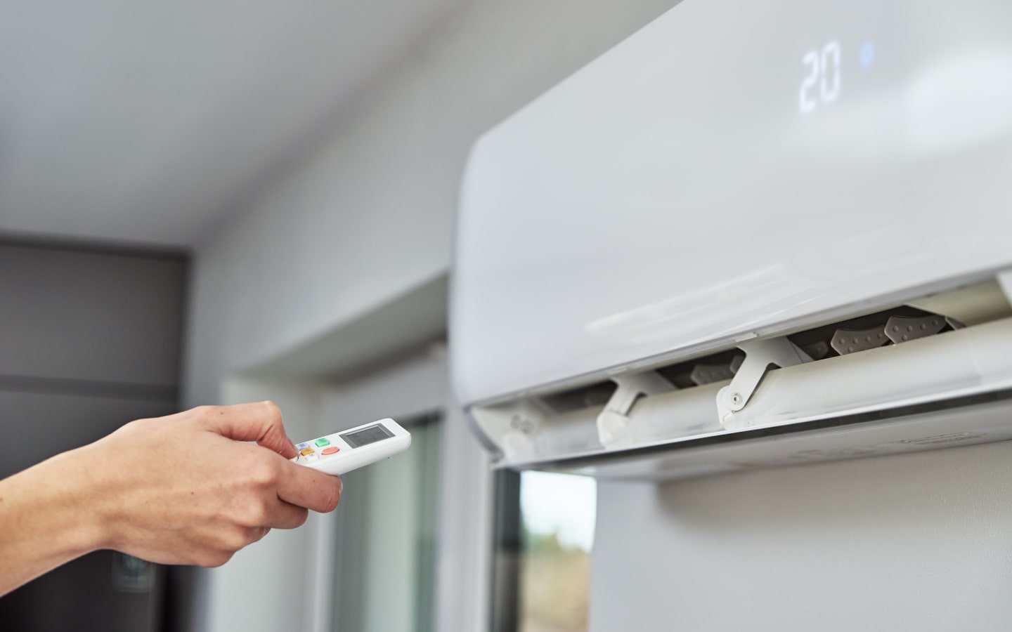 RHMH A person operates a wall-mounted air conditioner using a remote control, with the display showing a temperature setting of 20 degrees Celsius, expertly installed by an Air Conditioning Company in Timmins, Ontario. Heating And Air Conditioning