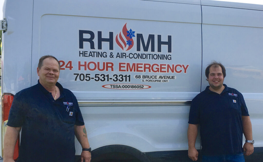 RHMH Two men standing in front of a white van displaying "RH & MH Heating & Air-Conditioning 24 Hour Emergency 705-531-3311" are wearing polo shirts with the company logo. This air conditioning company, based in Timmins, Ontario, offers reliable emergency services. Heating And Air Conditioning