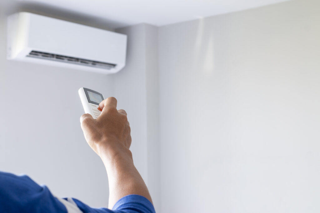 RHMH A person holds a remote control, aiming it at a wall-mounted air conditioning unit. Heating And Air Conditioning