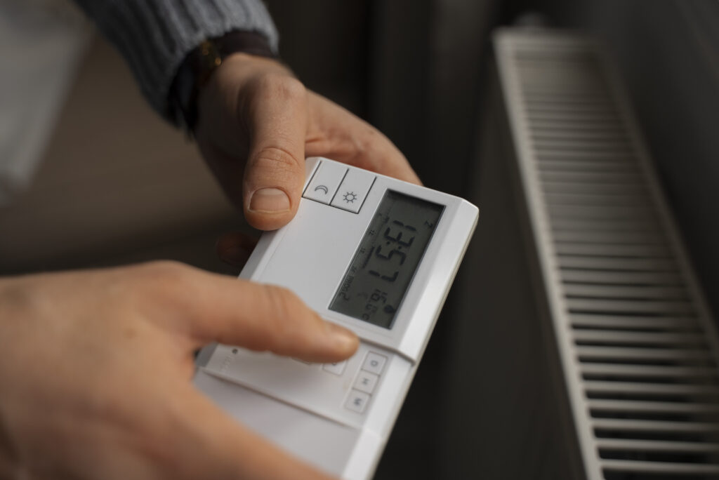 RHMH Person manually adjusting the temperature setting on a digital thermostat near a heater. Heating And Air Conditioning