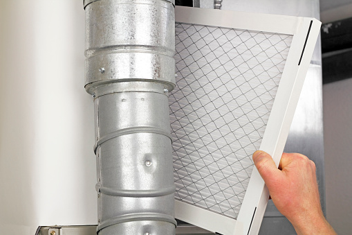 RHMH A person's hand is inserting a rectangular air filter into a metal air duct system, showcasing the meticulous work often performed by a top-notch heating company in Timmins, Ontario. Heating And Air Conditioning