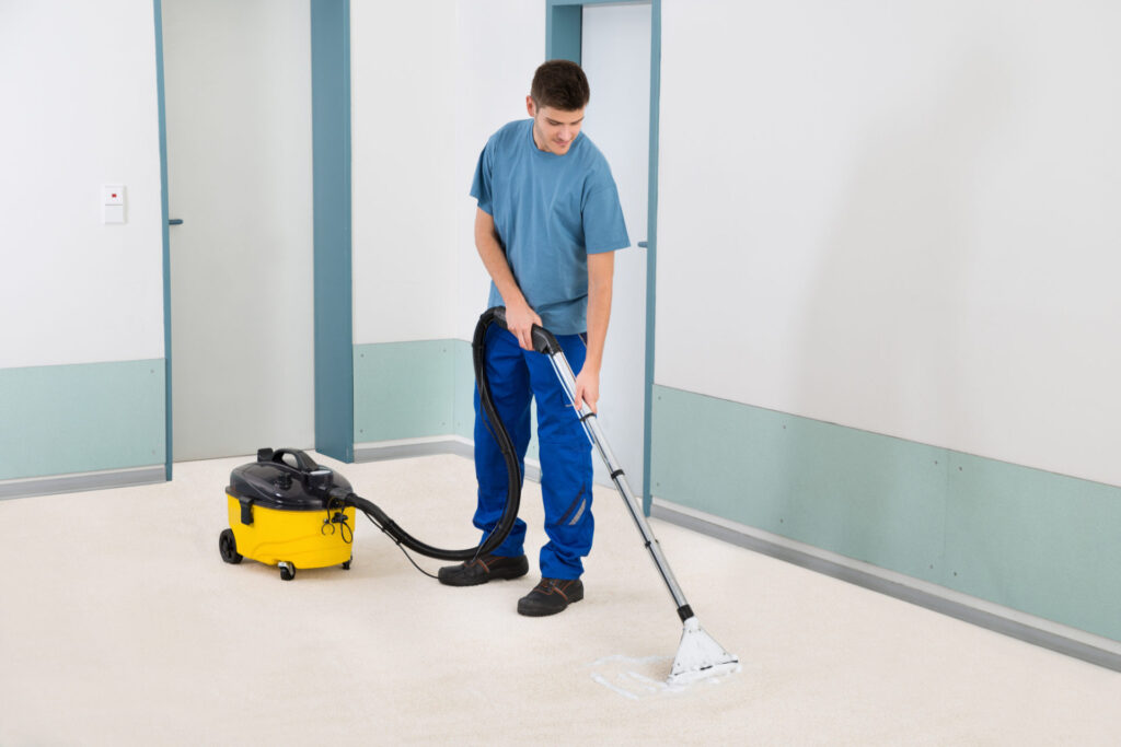 RHMH A person is cleaning a carpet with a yellow and black carpet cleaning machine in a hallway of an air conditioning company in Timmins, Ontario. They are wearing a blue shirt and blue pants. Heating And Air Conditioning