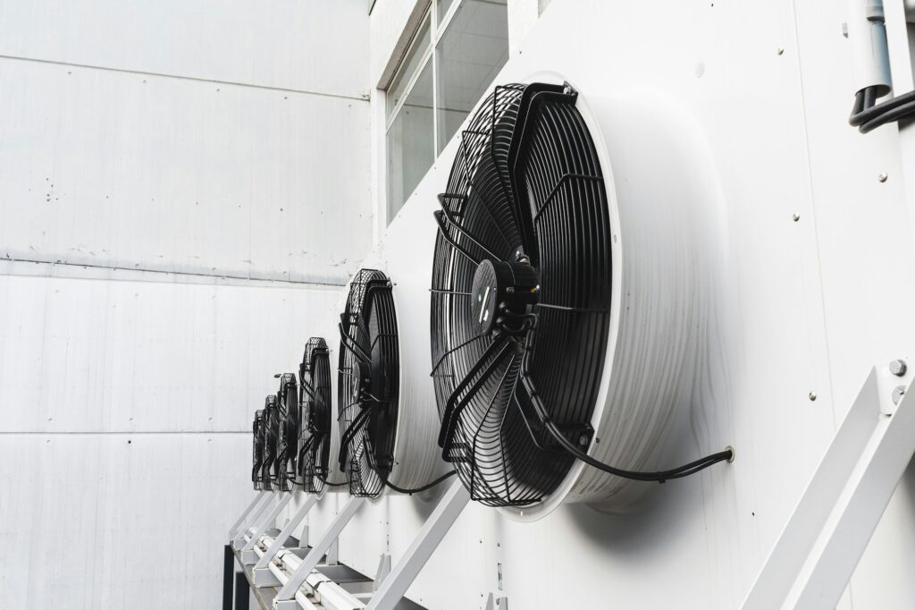 RHMH A row of industrial cooling fans mounted on the exterior wall of a building in Timmins, Ontario. The fans are aligned in a straight line on the pristine white wall, showcasing the meticulous installation by a reputable air conditioning company. Heating And Air Conditioning