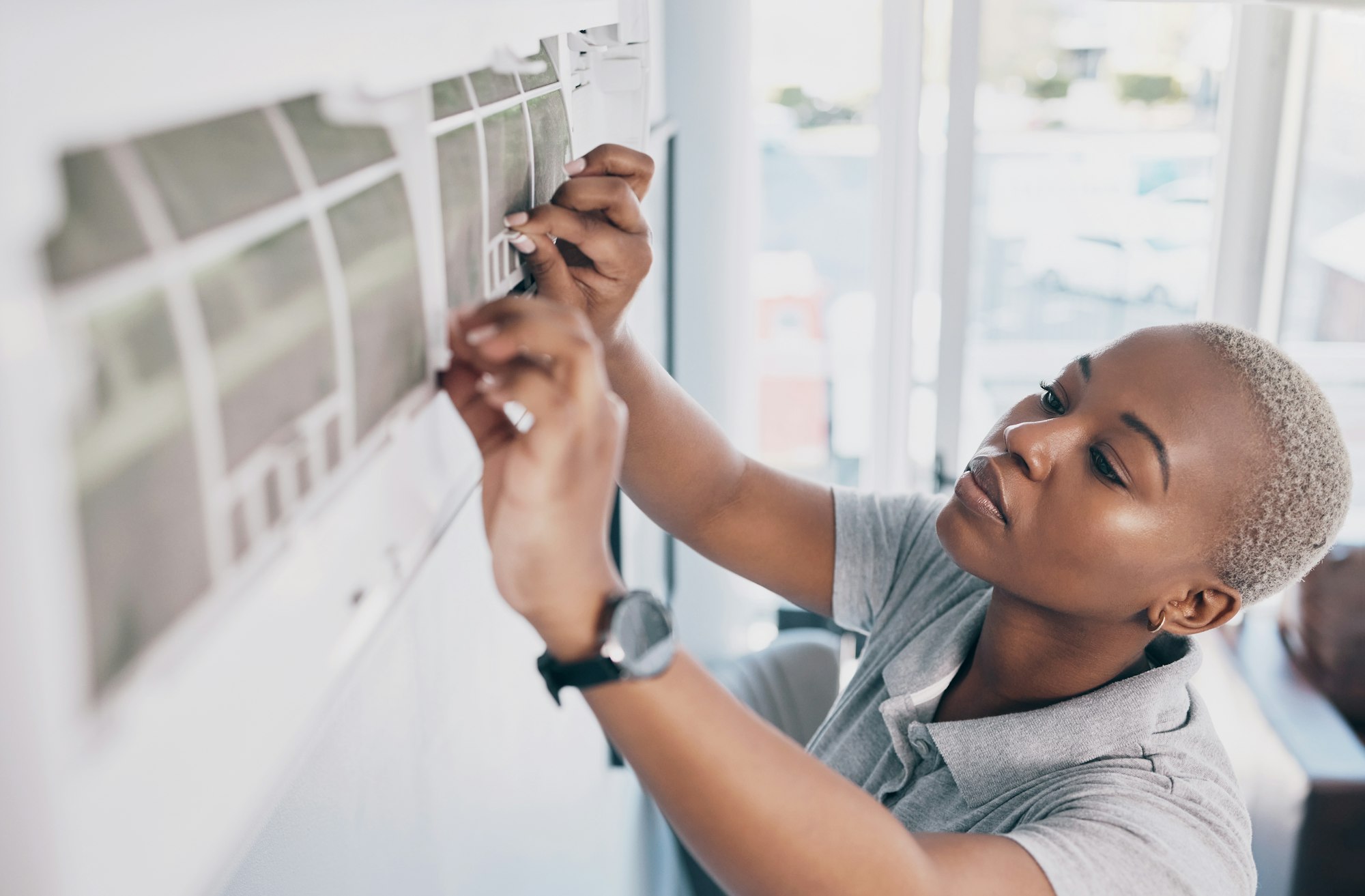 RHMH A person wearing a gray shirt, employed by an air conditioning company in Timmins, Ontario, adjusts the filter of an air conditioner mounted on a wall. The person is focused on the task and using both hands to handle the filter. Heating And Air Conditioning