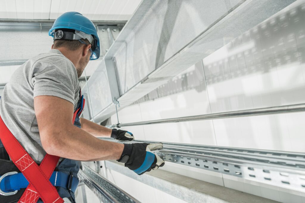 RHMH A worker in safety gear, including a helmet and harness, installs metal framework inside a building for an air conditioning company in Timmins, Ontario. Heating And Air Conditioning