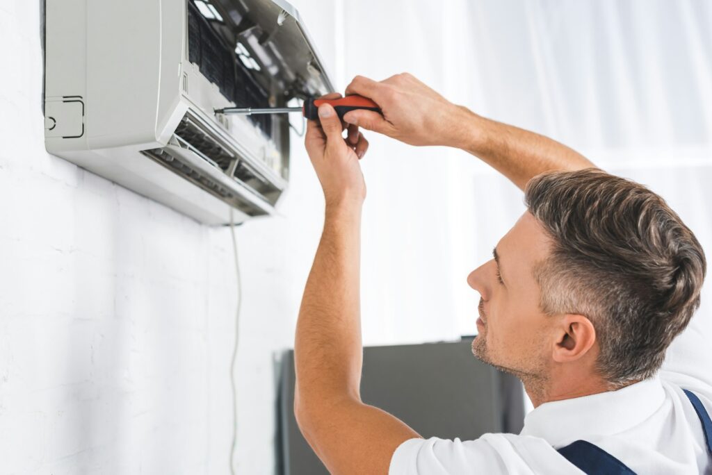 RHMH A person from a local Heating Company is using a screwdriver to repair or maintain an air conditioning unit on a wall in Timmins, Ontario. Heating And Air Conditioning
